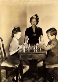 Plano general de Eva Rubinstein y Paul Rubinstein jugando al ajedrez mientras Aniela Rubinstein les observa
