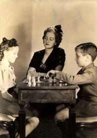 Plano general de Eva Rubinstein y Paul Rubinstein jugando al ajedrez mientras Aniela Rubinstein les observa