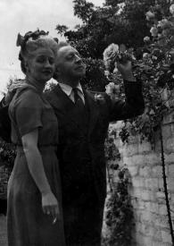 Plano general de Aniela Rubinstein posando junto a Arthur Rubinstein observando una flor