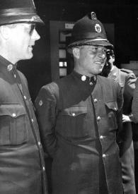 Plano medio de Arthur Rubinstein con sombrero y gafas de sol junto a dos hombres con uniforme