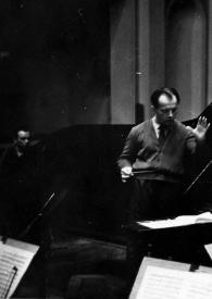Plano medio de Arthur Rubinstein (de espaldas) sentado al piano y Jerzy Katlewicz, con la batuta en la mano derecha, dirigiendo la orquesta