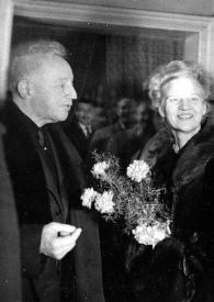 Plano general de Arthur Rubinstein (perfil derecho) y Aniela Rubinstein con un ramo de flores en las manos posando