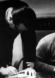 Plano medio de Arthur Rubinstein en una entrevista, mirando a la periodista (de espaldas). Dos hombres tomando notas