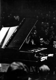Plano general de Arthur Rubinstein (perfil izquierdo), sentado al piano, detrás  y delante de él, el público