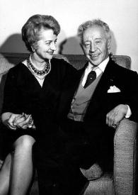 Plano general de Aniela Rubinstein (perfil derecho) y Arthur Rubinstein sentados en un sillón, cogidos de la mano, posando