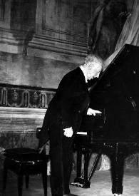 Plano general de Arthur Rubinstein (perfil derecho) saludando al público, de pie junto al piano