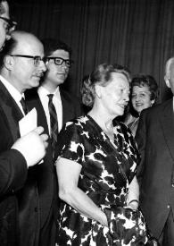 Plano medio de Arthur Rubinstein (perfil izquierdo) conversando con varias personas, al fondo Aniela Rubinstein