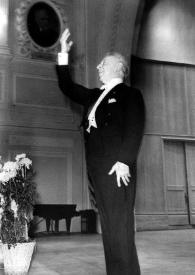 Plano general de Arthur Rubinstein (medio perfil izquierdo), de pie en el escenario, saludando al público