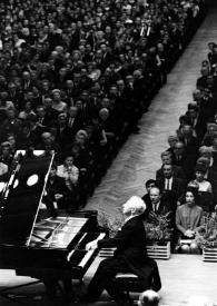 Plano general de Arthur Rubinstein (perfil izquierdo) sentado al piano, con el público al fondo. Fotografía tomada desde el escenario