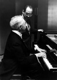 Plano medio de Arthur Rubinstein (perfil derecho) sentado al piano junto a sentado