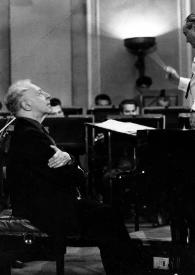 Plano medio de Arthur Rubinstein (perfil derecho) sentado al piano delante de János Ferencsik dirigiendo la orquesta