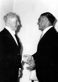 Plano medio de Arthur Rubinstein (perfil derecho) y un hombre (perfil izquierdo) estrechándo las manos.