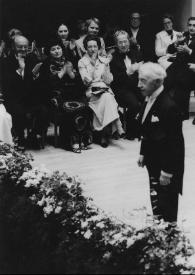 Plano general de Arthur Rubinstein (perfil izquierdo) de pie saludando al público a su espalda