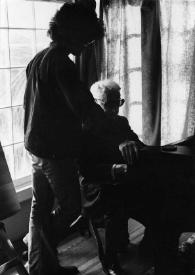 Plano general de John Rubinstein de pie (de espaldas) junto al piano y de Arthur Rubinstein sentado al piano. Fotografía tomada a contraluz