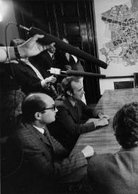 Plano general de la mesa de reuniones: entre ellos, Henryk Czyz, Arthur Rubinstein y los altos cargos del ayuntamiento charlando. Alrededor de la mesa los periodistas sostienen los micrófonos y las cámaras