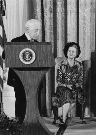 Plano general de Arthur Rubinstein hablando en el atril presidencial, Aniela Rubinstein, Betty Ford y Gerald Ford, Presidente de Estados Unidos, sentados detrás escuchándole