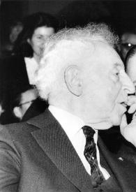 Plano medio de Arthur Rubinstein (perfil derecho) sentado entre el público charlando con Raymond Barre (Primer Ministro)