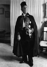 Plano general de Arthur Rubinstein posando con el traje de académico, con capa, sombrero y la mano sujetando la empuñadura de la espada que cuelga de su cintura.