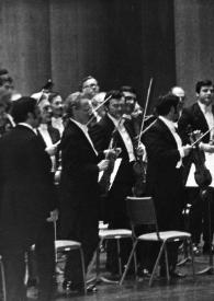 Plano medio de Arthur Rubinstein, de pie, saludando al público junto al piano, detrás la orquesta