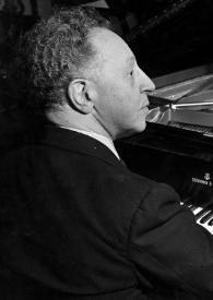 Plano medio de Arthur Rubinstein (perfil derecho) de espaldas sentado al piano