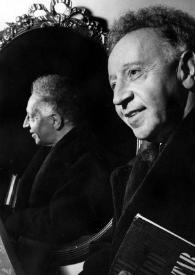 Plano medio de Arthur Rubinstein (medio perfil izquierdo) posando junto a un espejo donde también se ve su rostro