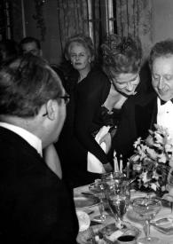 Plano general de André Segovia (de espaldas con gafas negras), una mujer, Aniela Rubinstein, Arthur Rubinstein y Alice Hay observando algo que se encuentra en la mesa donde él está sentado