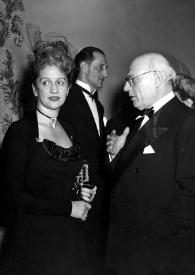Plano general de Aniela Rubinstein y Sol Hurok (perfil izquierdo) charlando, detrás Basil Rathbone.