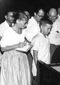 Plano medio de un niño mirando a Arthur Rubinstein sentado al piano posando rodeado de personas