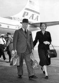 Plano general de Aniela y Arthur Rubinstein posando mientras caminan por el aeropuerto, al fondo un avión