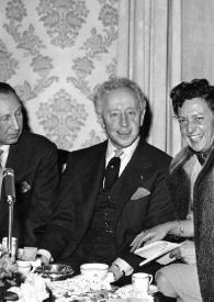 Plano medio de Arthur Rubinstein posando sentado en una mesa con otras tres personas