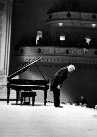 Plano general lateral del escenario, Arthur Rubinstein (perfil derecho), de pie, saludando al público, que está aplaudiendo, junto al piano