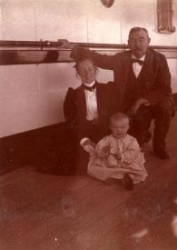 Plano general de tres compañeros de viaje: una mujer, un hombre, un bebé posando sentados en el suelo de la cuebierta del barco