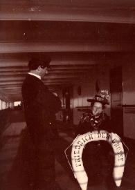 Plano general de un hombre y el Capitán Eichel observando a la Señora de Rosentower posando con el salvavidas