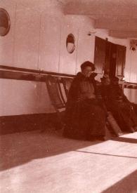 Plano general de la Señora Rosentower posando sentada junto a una mujer que está charlando de espaldas con la Señora Hartzell, a la derecha de la foto un hombre paseando por cubierta