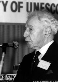 Plano medio de Arthur Rubinstein (perfil izquierdo) hablando a través de un micrófono durante la conferencia