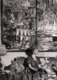 Plano general de Aniela Rubinstein y Elias Kanarek charlando sentados en un sillón. En la pared tres cuadros de Elias Kanarek que representan tres momentos de la vida de Arthur Rubinstein, de izquierda a derecha: París, Nueva York y Hollywood