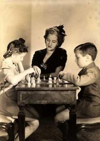 Plano general de Eva Rubinstein y Paul Rubinstein jugando al ajedrez mientras Aniela Rubinstein les observa