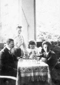 Plano general de Isaac Rubinstein y Felicja Heiman Rubinstein (padres de Arthur Rubinstein), una niña y Arthur Rubinstein sentados en una mesa jugando al ajedrez