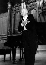 Plano general de Arthur Rubinstein (medio perfil izquierdo), de pie en el escenario, saludando al público