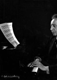 Plano medio de Arthur Rubinstein (perfil izquierdo) sentado al piano observando unas partituras