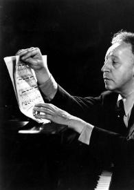 Plano medio de Arthur Rubinstein pasando las hojas de una partitura sentado al piano