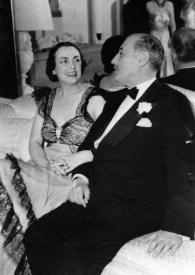 Portada:Plano general de Gladys Peabody y Sir Victor Sassoon (perfil izquierdo) charlando, sentados en un sofá