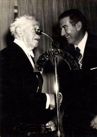 Portada:Plano medio de Arthur Rubinstein charlando con un hombre junto al micrófono