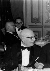 Portada:Plano medio de Sol Hurok charlando con Arthur Rubinstein, sentados en una mesa, junto a una mujer