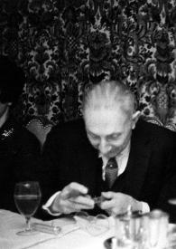 Portada:Plano medio de Arthur Rubinstein (perfil izquierdo), sentado a la mesa, con un puro en la mano junto a un hombre