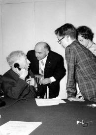 Portada:Plano medio de Arthur Rubinstein, hablando por teléfono, junto a un hombre, John Rubinstein y Alina Rubinstein
