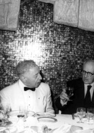 Portada:Plano medio de Arthur Rubinstein, en una comida, conversando con otras personas