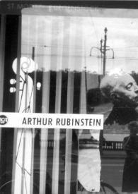 Portada:Plano general de Aniela Rubinstein, reflejada en el escaparate de la tienda, mientras hace una fotografía a Arthur Rubinstein, que está sentado al piano en el interior
