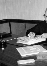 Portada:Plano medio de Arthur Rubinstein, sentado en una mesa, firmando unas hojas
