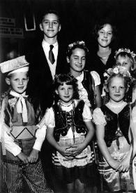 Portada:Plano general de John Rubinstein y Alina Rubinstein posando con varios niños con traje típico polaco